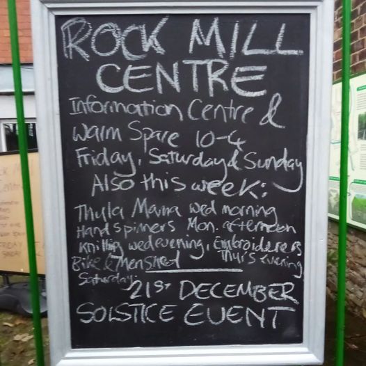 A chalkboard sign reads: Rock Mill Centre. Information Centre & Warm Space 10-4 Friday, Saturday, Sunday. Also this week: Thula Mama Wednesday morning, Hand spinners Monday afternoon, knitting Wednesday evening, Embroiderers Thursday evening, Bike & Men's shed Saturday. 21st December Solistice Event