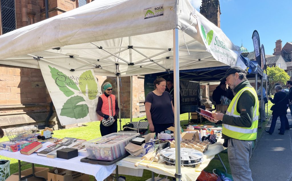 Sustainable Carlisle's free stall, two tables under a gazebo in the sunshine, is heavily laden with household items, books, toys and more that residents would like to pass on for free. 