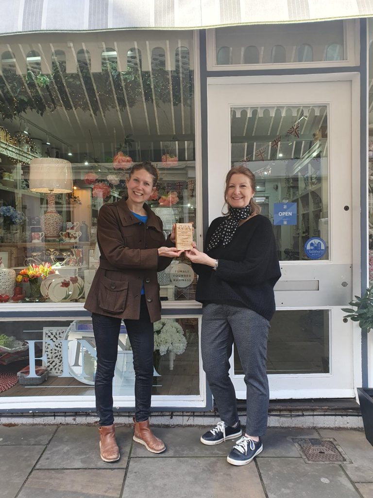 Sophia (left) from Salisbury Transition City hands over a small wooden trophy to the owner of local business, Casa Fina in front of the shop window. 