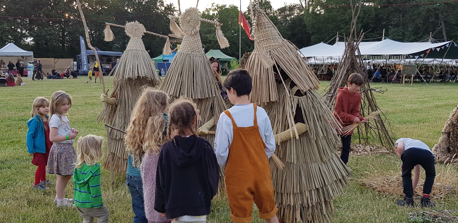 Three 'mummers' dressed in straw outfits and head dresses which mask their faces hand out stalks of grain to children at the Land Skills Fair