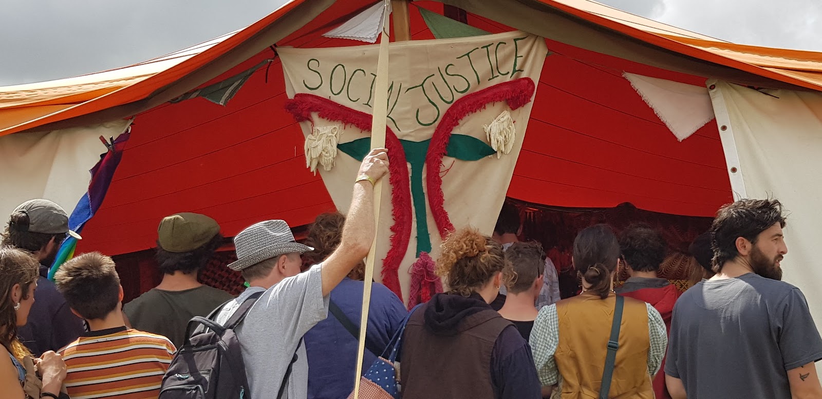 People spill out of a red and white tent, labelled Social Justice. 