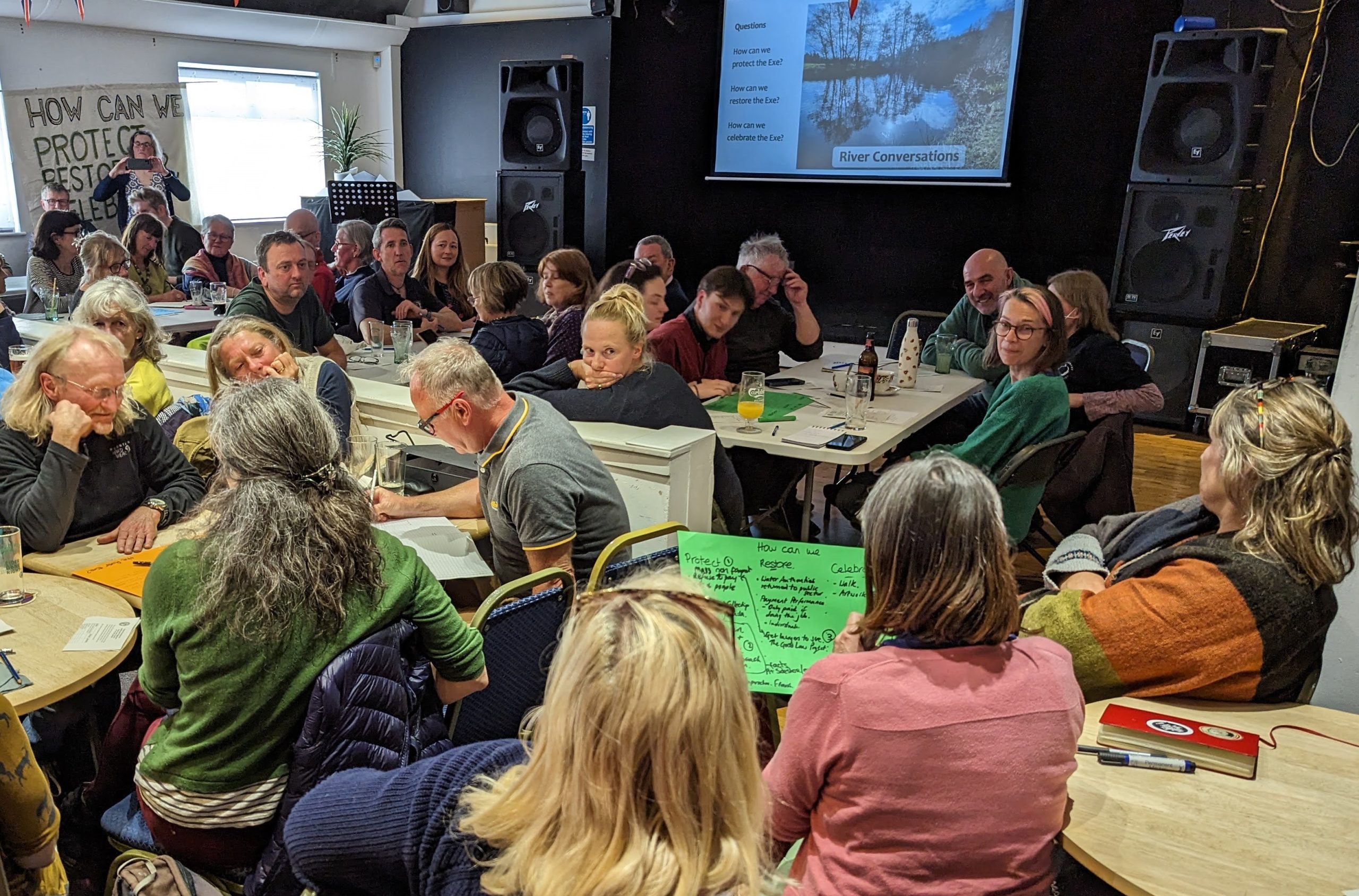 People gather at tables in a community hall to discuss how to protect, celebrate and restore the River Exe.
