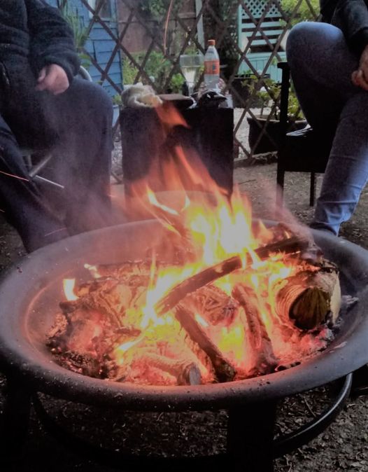 A roaring fire in a fire pit, as a couple of people warm their legs by the blaze. 