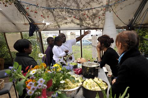 A group gather around potatoes being prepared in big pots and flowers grown on site on a table in the historic glasshouse of the Grow Heathrow site. 