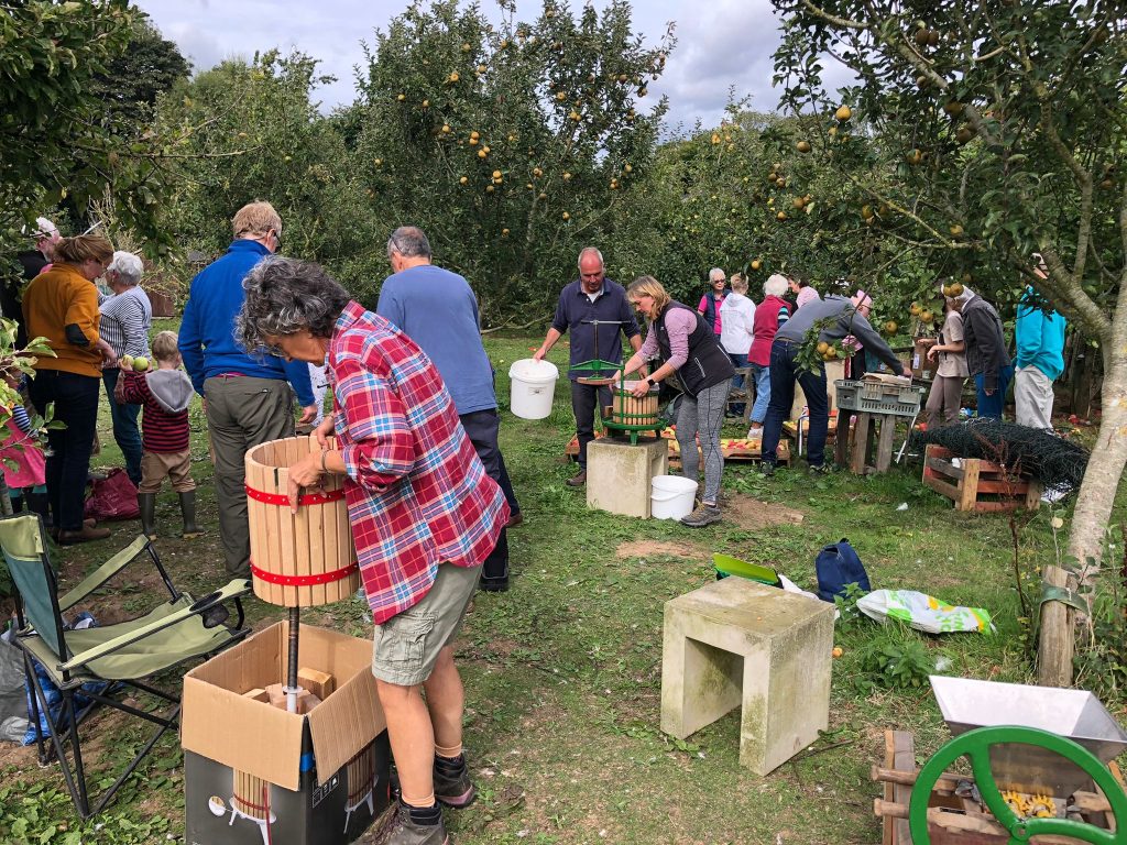 People are gathered at the farm's community orchard to prepare and press the apples into juice. 