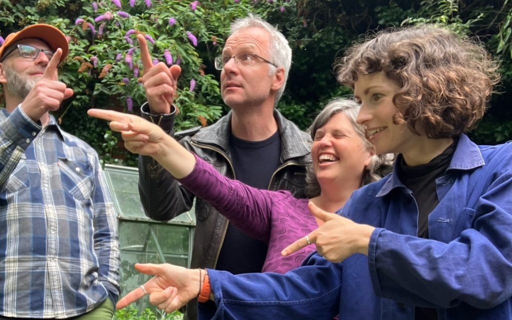 Phil, Rich, Jess and Joanna stand pointing in various different directions. Behind them is an old greenhouse and a wall of ivy. 